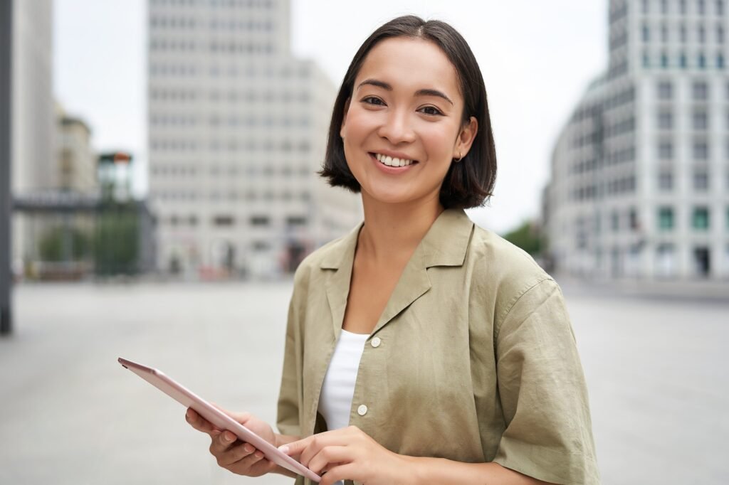 Young smiling asia woman with tablet, standing on street in daylight